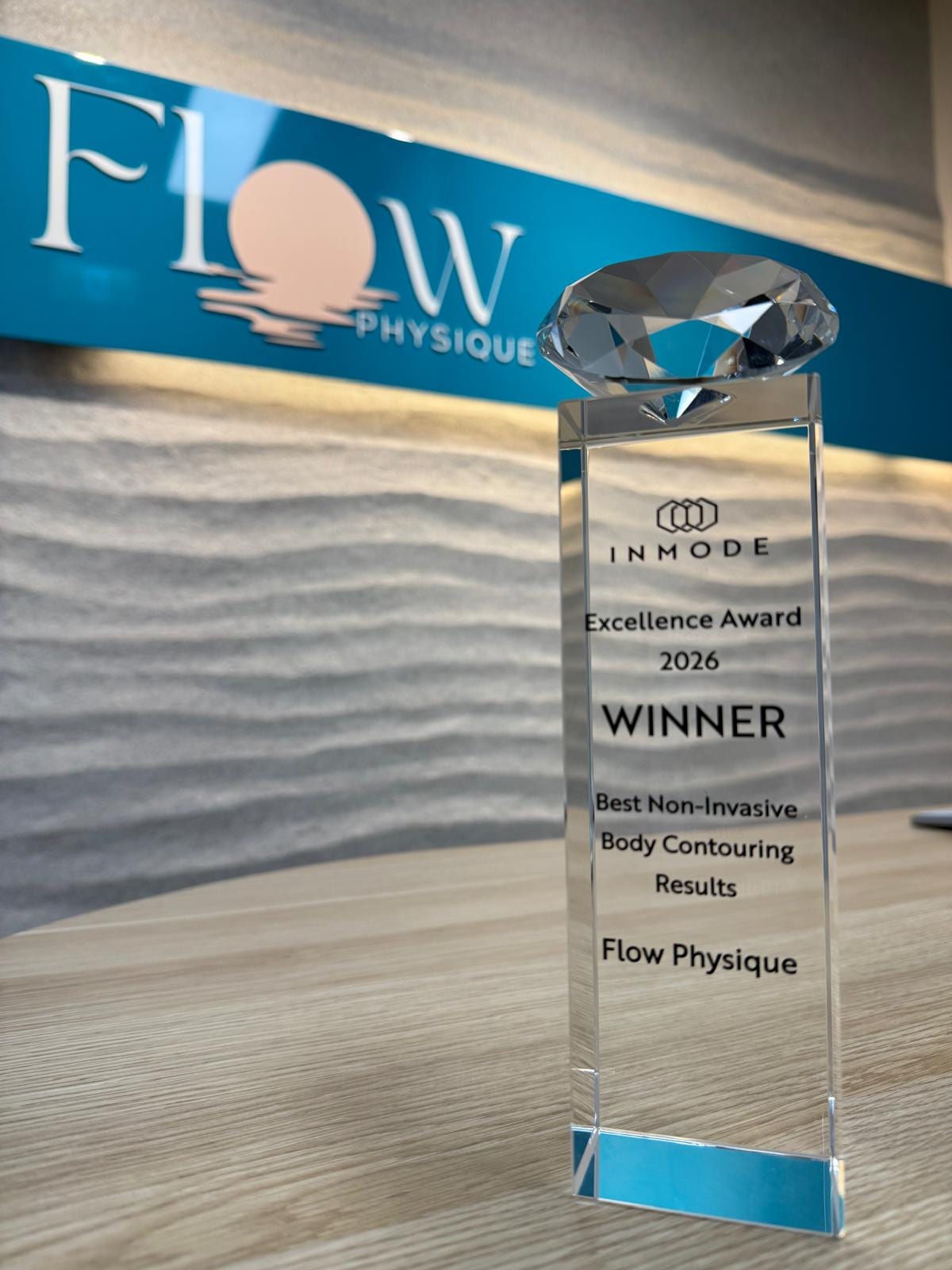 The InMode Excellence Award 2026 trophy at the Flow Physique reception desk, engraved with Winner, Best Non-Invasive Body Contouring Results, Flow Physique